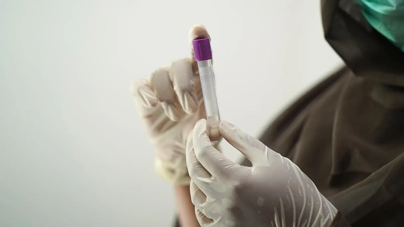 Behandschuhte Hände halten ein Blutröhrchen mit violettem Deckel