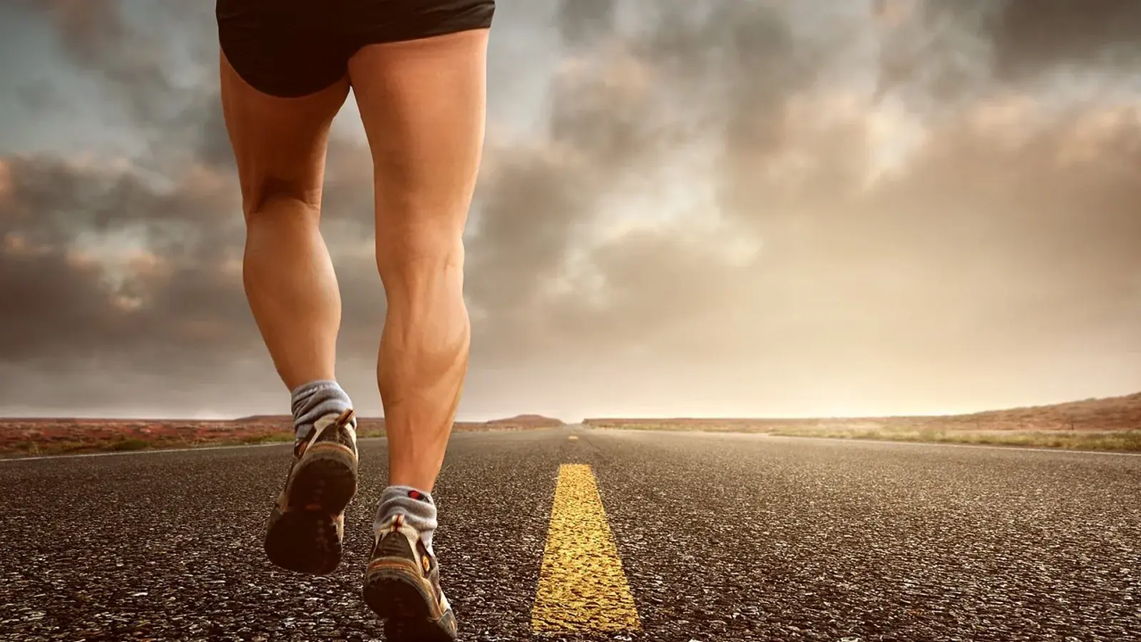 Beine eines Läufers in Laufschuhen auf einer Landstraße unter bewölktem Himmel
