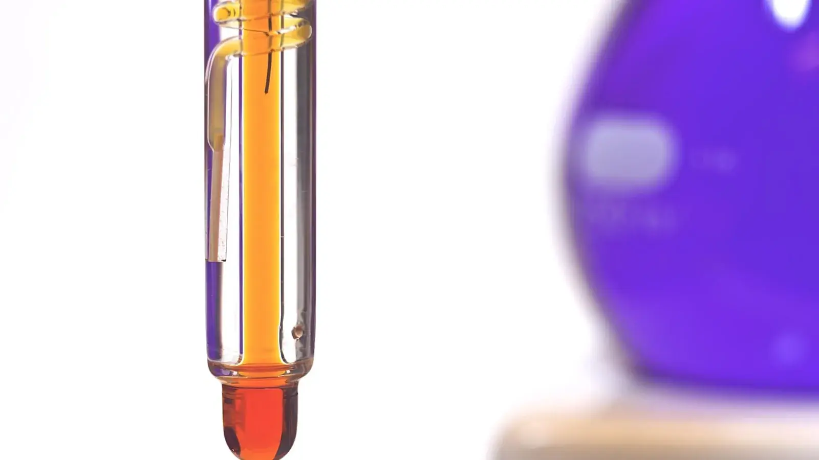 Messelektrode mit orangefarbener Flüssigkeit im Labor, dahinter unscharf ein violetter Glaskolben